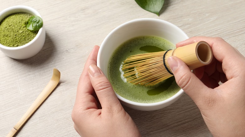 Person whisking matcha in white bowl