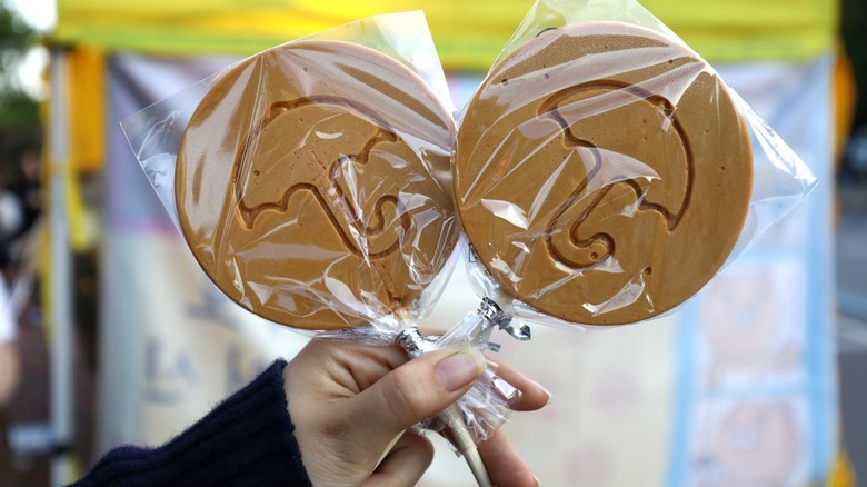 Two plastic-wrapped dalgona lollipops held by a single hand