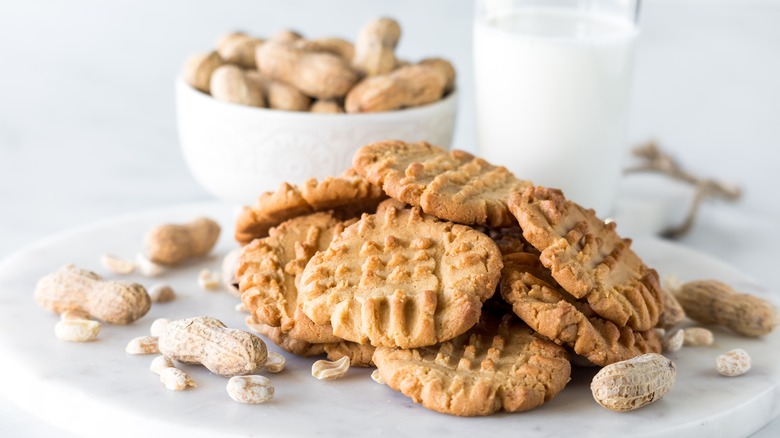 A plate of peanut butter cookies surrounded by peanuts and a glass of milk