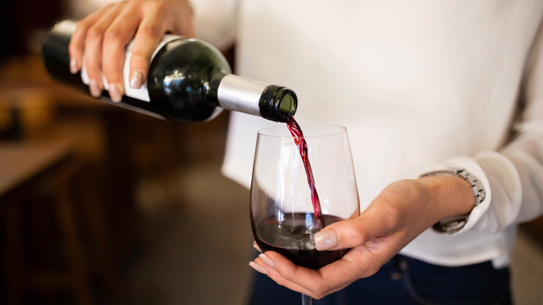 person pouring red wine into a glass