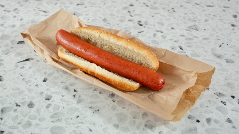 A plain, perfect-looking hot dog sits on a brown wrapper against a white granite background