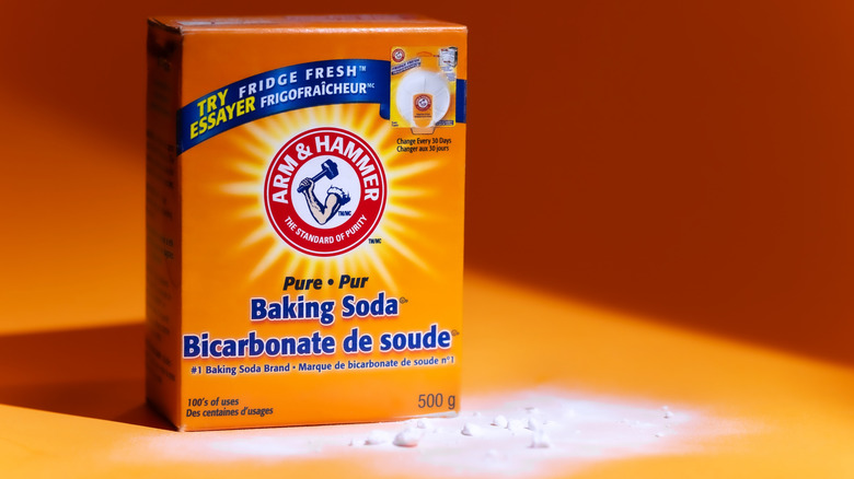 A box of Arm & Hammer baking soda sits on an orange surface, with a small amount of baking soda spilled around the box