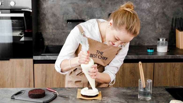 A woman using a piping bag to frost a dessert.