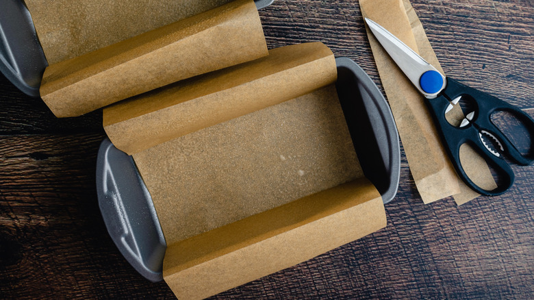 Two baking pans lined with parchment paper sitting next to a pair of scissors.