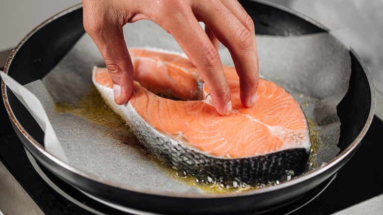 Cooking salmon steak on parchment paper in skillet