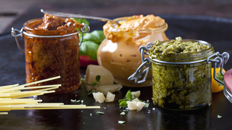 Various pasta sauces in jars next to raw spaghetti noodles