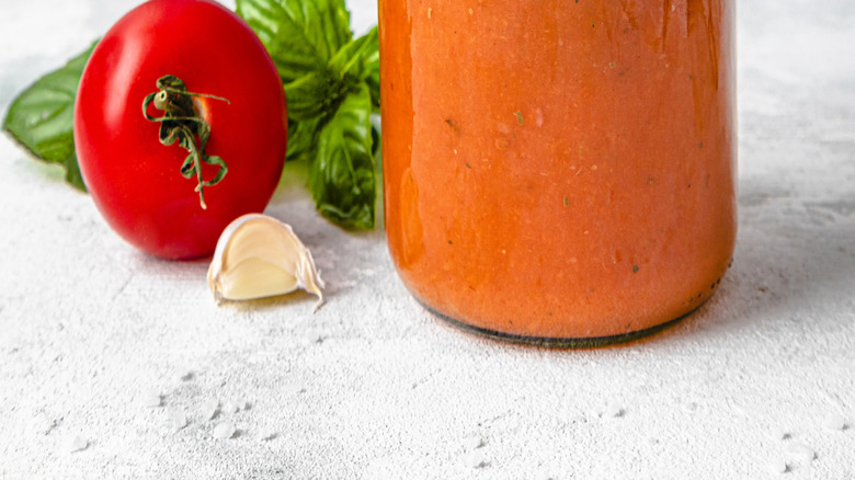 Hand putting lid on creamy tomato sauce in a jar