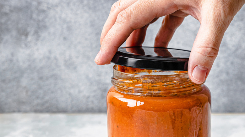 Hand putting lid on creamy tomato sauce in a jar