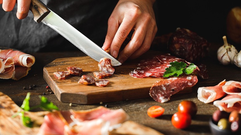 Hands using knife to cut charcuterie on cutting board