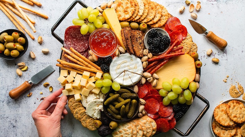 Hand grabbing a cube of cheese off a colorful charcuterie board filled with fruit, crackers, meat, and cheese