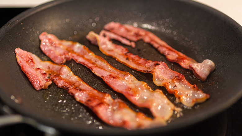 Four slices of bacon getting cooked on a black skillet