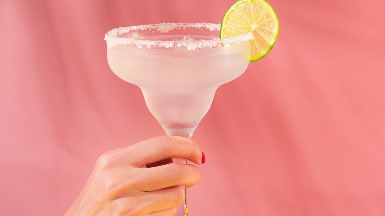 Woman holding margarita against pink backdrop