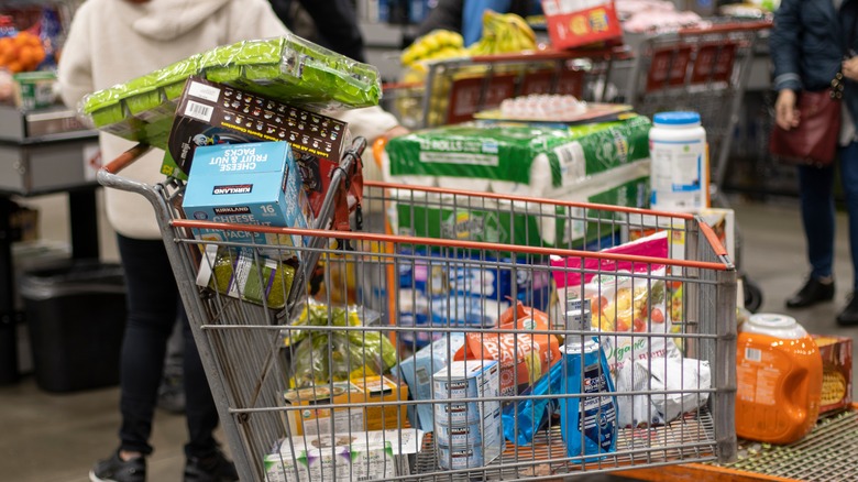 A cart full of items from Costco's Kirkland Signature brand sits in a busy store