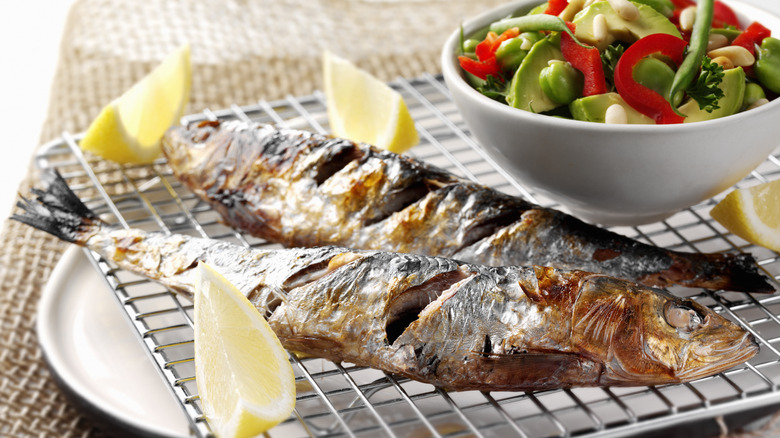 Two deeply scored grilled fish sit on a metal rack with lemon wedges