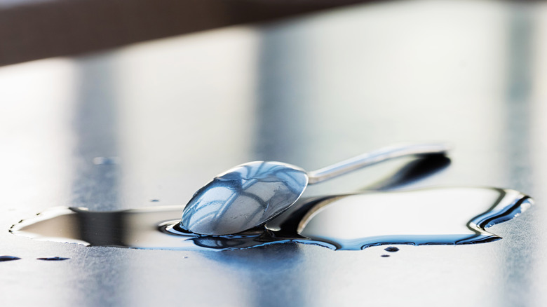 A dropped spoon has landed in a pool of water or soup on a table or floor.