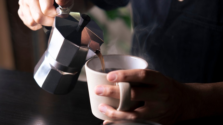 Pouring hot coffee from moka into mug