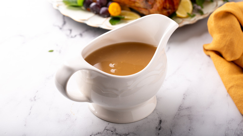 A white ceramic container filled with gravy sits on a marbled surface.