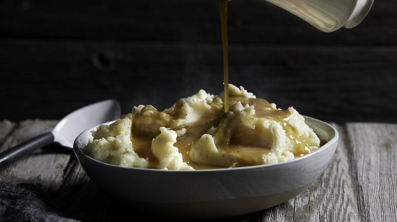 Gravy being poured over mashed potatoes in a bowl