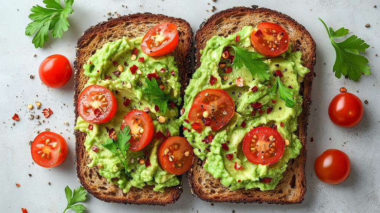 Avocado and tomato on toast has fresh tomatoes and chili flakes sprinkled on the side.