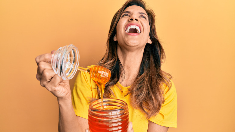 A person with long hair maniacally laughs while holding honey