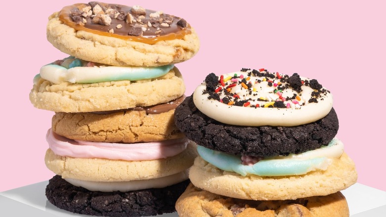 Two stacks of assorted Crumbl cookies with pink background
