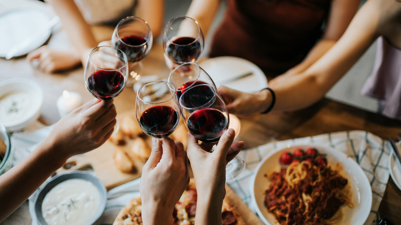 people clink glasses of red wine over a dinner table
