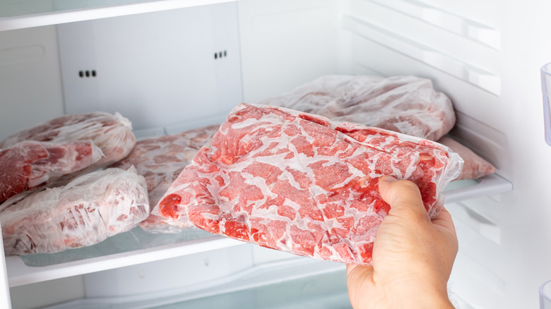 A hand pulling a package of frozen meat out of the freezer.