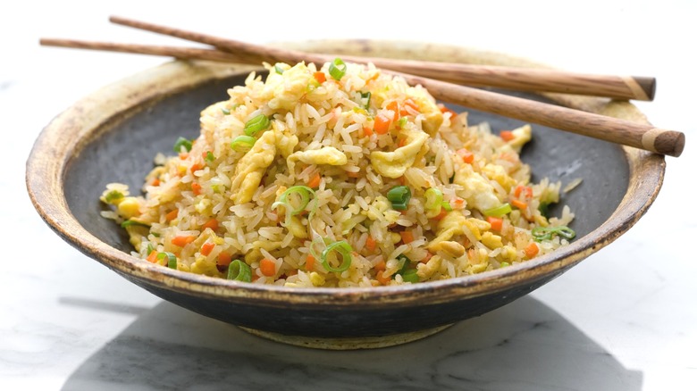 A bowl of fried rice with egg has chopsticks crossed on top of it