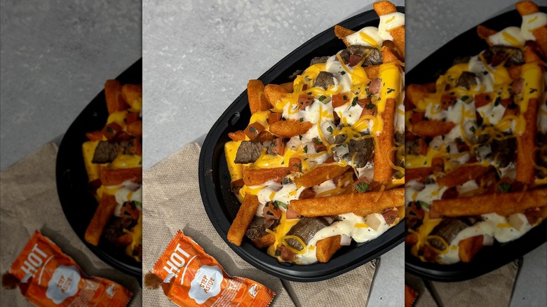 A bowl of garlic steak nacho fries sits beside a Taco Bell hot sauce packet