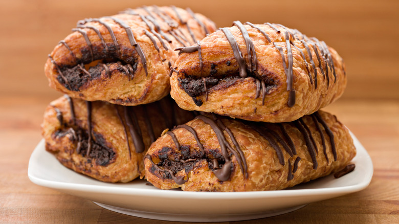 Chocolate croissants on white plate with wooden background.