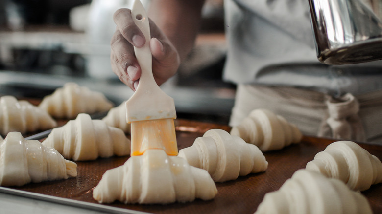 A baker brushes butter on top of rolled croissants, waiting to be baked