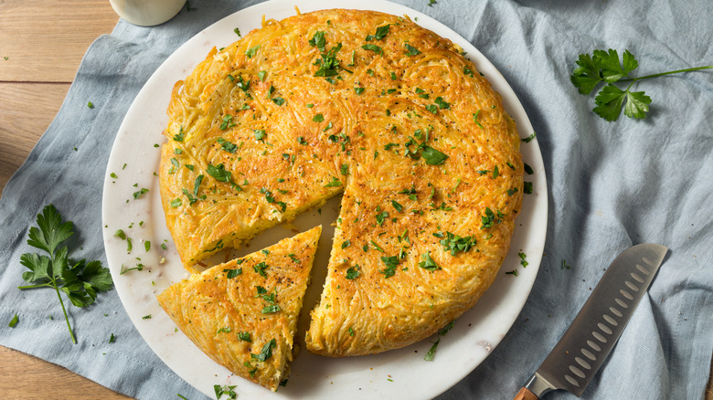 Spaghetti frittata on white plate with one slice cut out