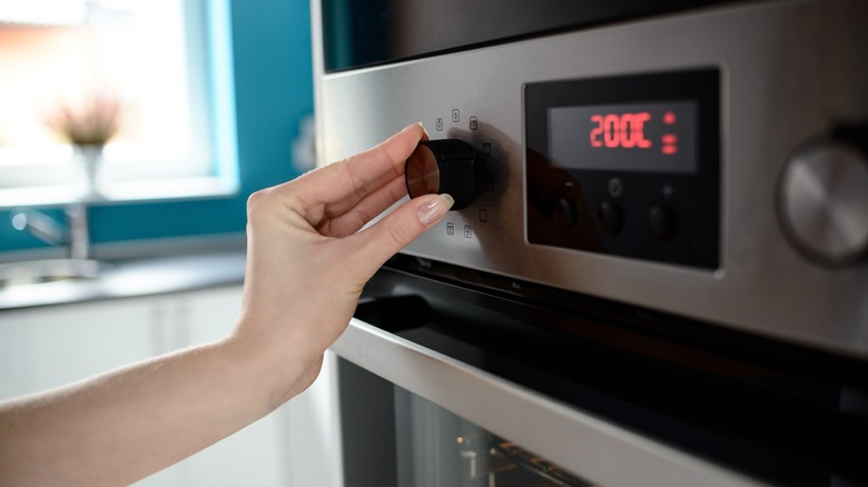 A hand adjusting an oven's temperature dial