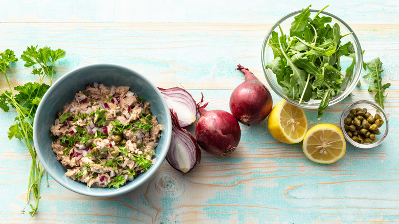 Tuna salad in a bowl plus onions, lemon, capers, and herbs