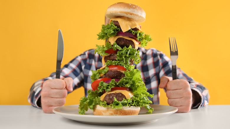 Towering burger with man with knife and fork