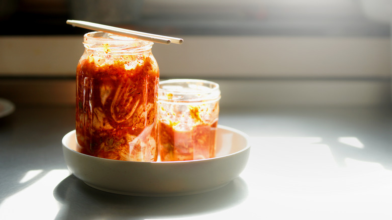 Two jars of kimchi sit on a kitchen counter, bathed in sunlight