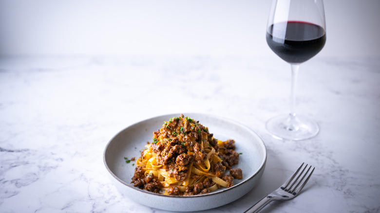 Bowl of meat ragu and a dark red wine on a white marble background