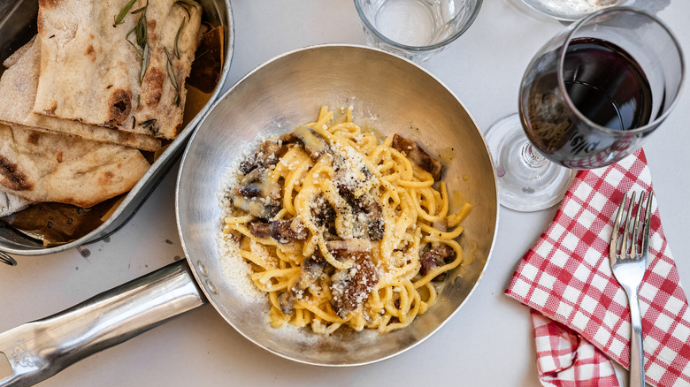 A pan of carbonara with flatbread and a glass of red wine