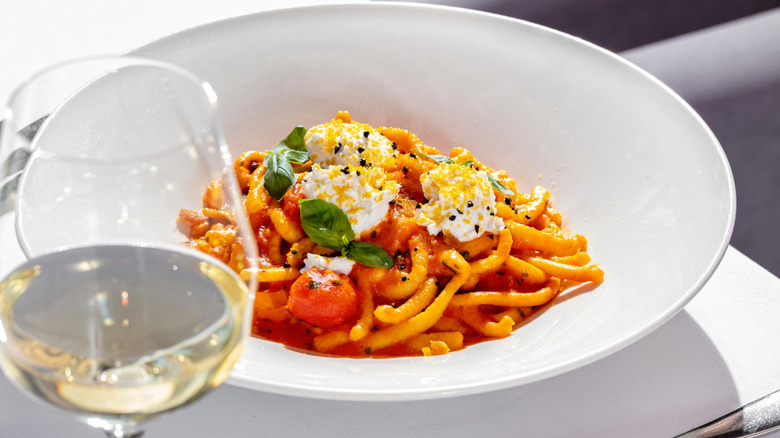 A bowl of vodka sauce with ricotta and basil and a glass of white wine foregrounded