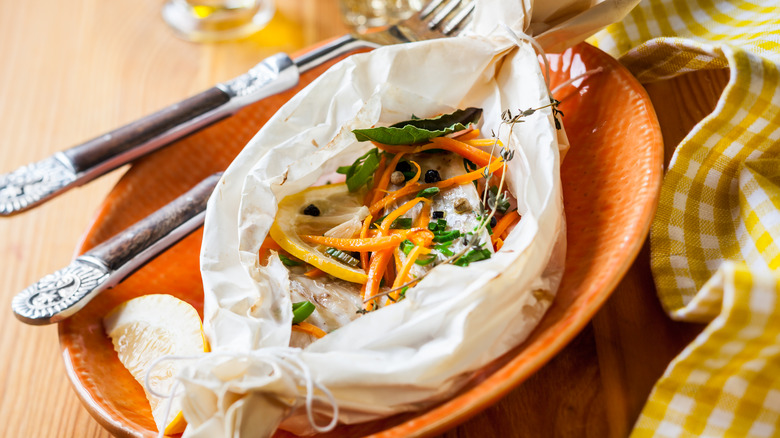 fish and veggies cooked inside parchment paper on an orange plate