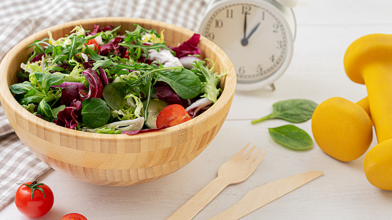 A wooden bowl filled with mixed salad sits on a counter.