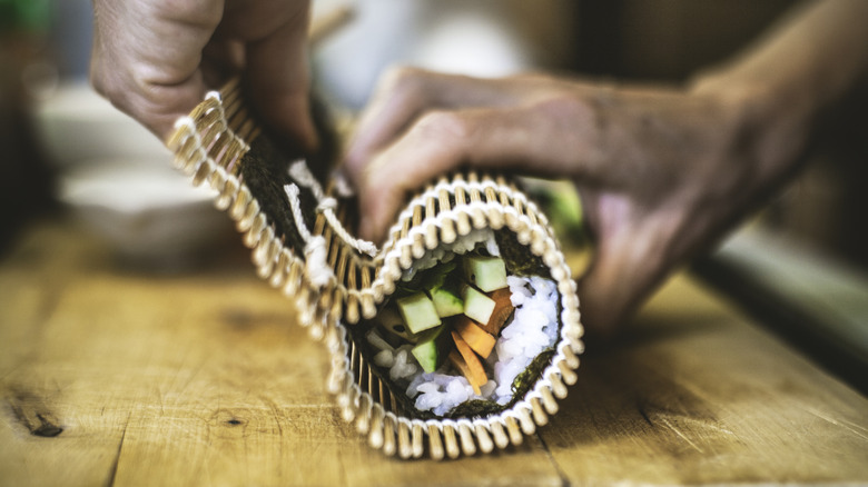 A sushi chef rolls a maki roll with a bamboo mat.