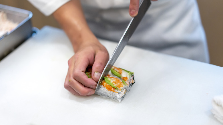 A chef slices sushi rolls on a white cutting surface.