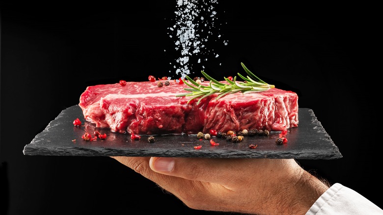 Person sprinkling salt on a raw steak