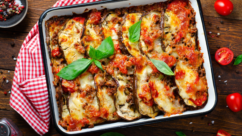 Eggplant parmigiana in a rectangular baking dish with tomato sauce and melted cheese on a wooden surface with cherry tomatoes on the side