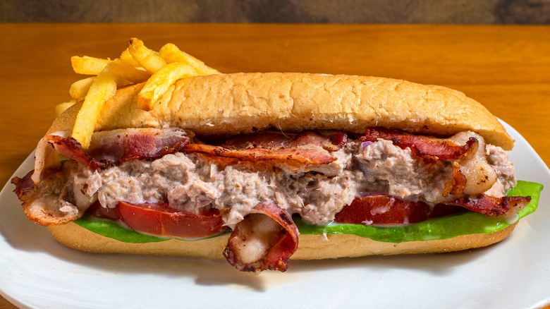 Fries and tuna salad sub sandwich with bacon, lettuce, and tomato on a white plate