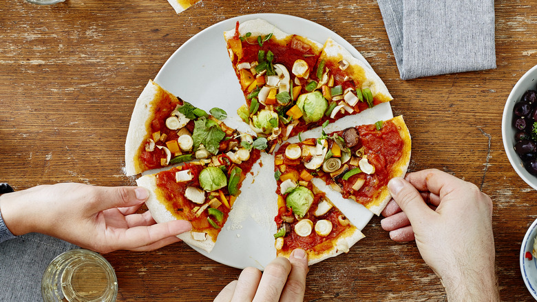 Hands reaching for slices of vegan pizza