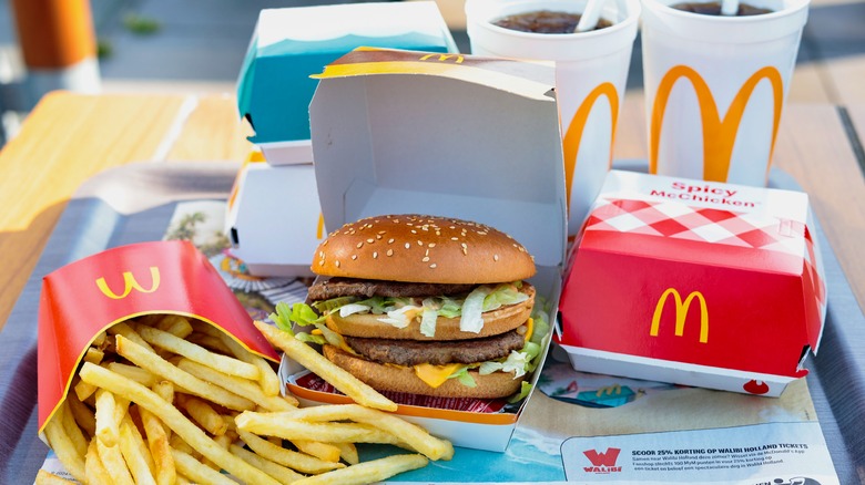 Tray of McDonald's food, including Big Mac in open box, French fries, two sodas, a Spicy McChicken, and two other sandwiches in background