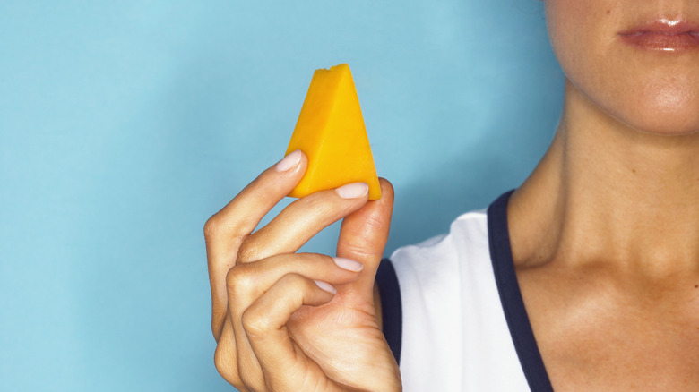 close up of woman holding a wedge of cheddar cheese