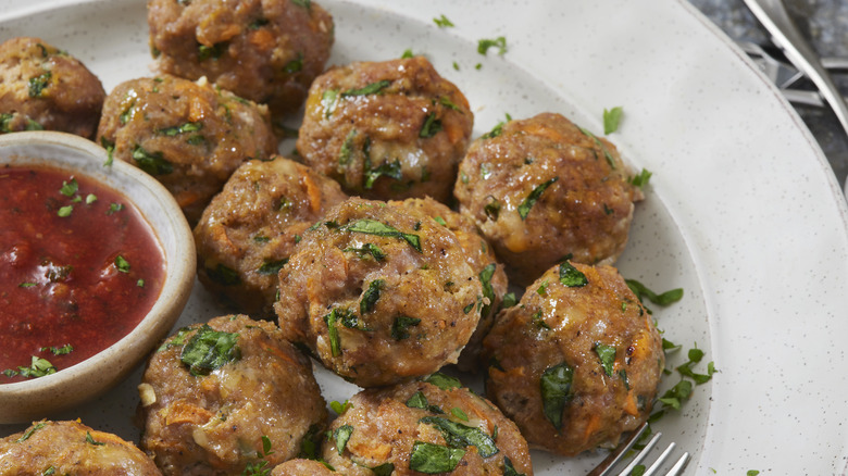 Cooked turkey meatballs with minced herbs next to dish of red sauce